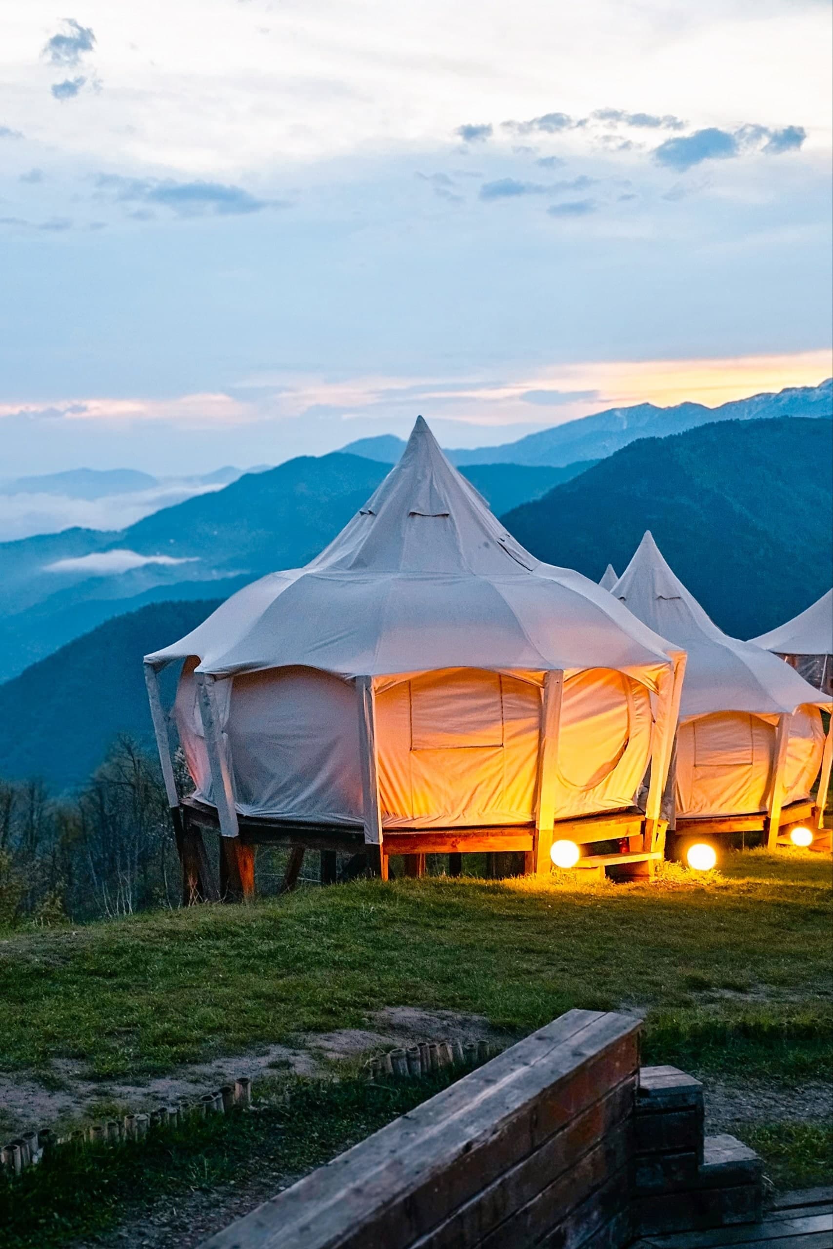 Illuminated glamping tents on a mountain with a cloudy sky at dusk, Glamping Tago, Georgia.